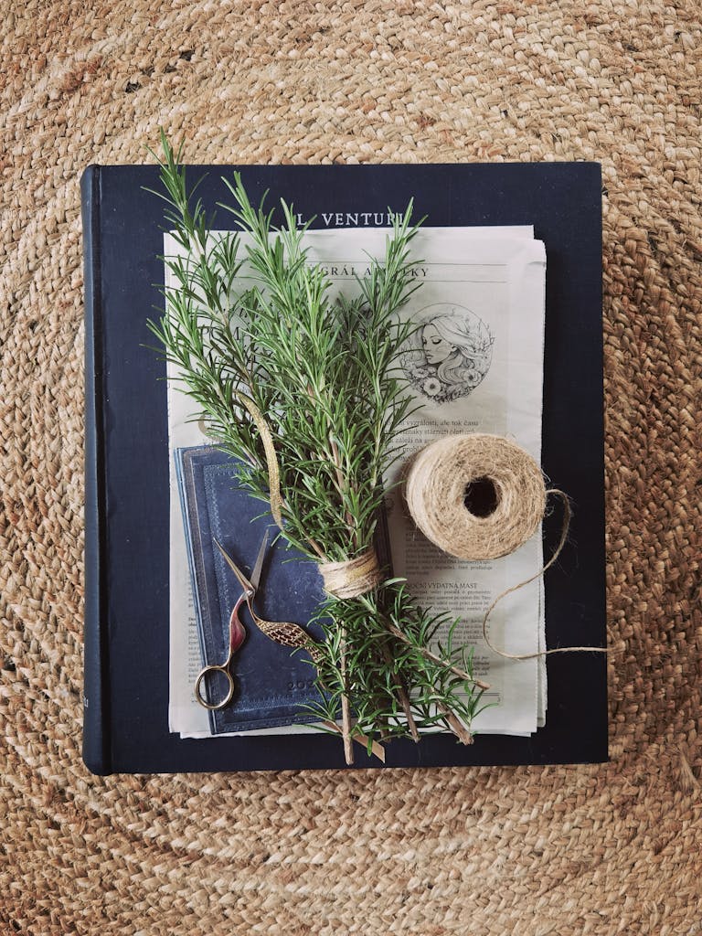 A bundle of fresh rosemary, scissors, and twine on a rustic mat, evoking a cozy artisanal feel.