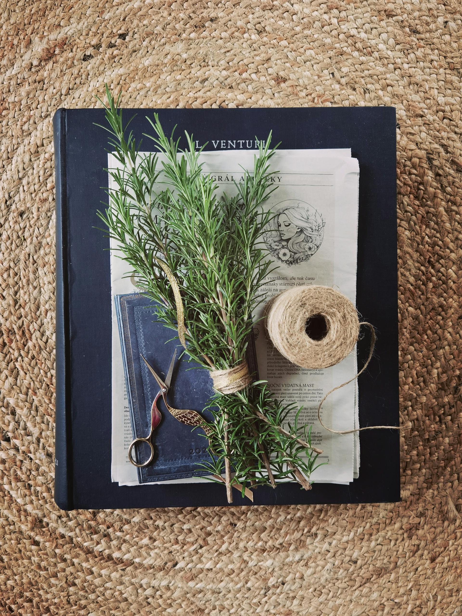 A bundle of fresh rosemary, scissors, and twine on a rustic mat, evoking a cozy artisanal feel.